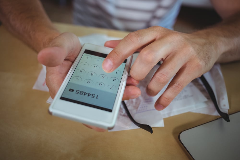 Mid section of man calculating bills on mobile phone