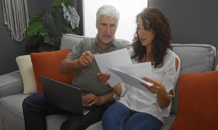 Couple looking at paperwork sitting on couch with laptop