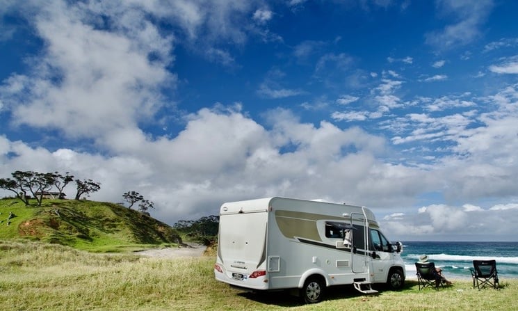 Motorhome parked on grass at beach with camping chairs